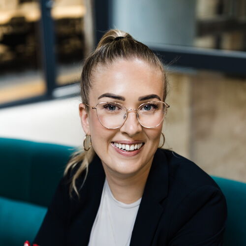 Lisa Garcia in schwarzem Blazer auf grünem Sofa im Coworking Space