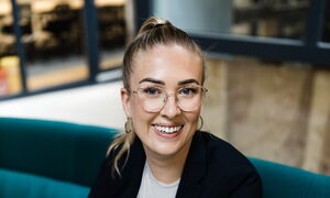 Lisa Garcia in schwarzem Blazer auf grünem Sofa im Coworking Space