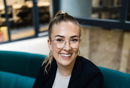 Lisa Garcia in schwarzem Blazer auf grünem Sofa im Coworking Space