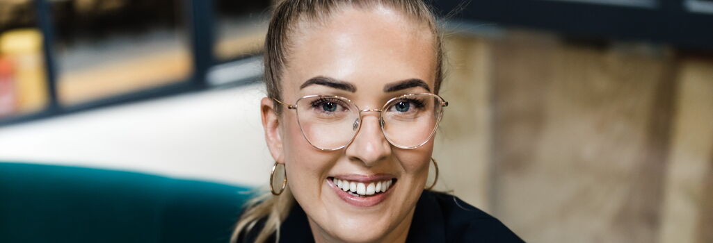 Lisa Garcia in schwarzem Blazer auf grünem Sofa im Coworking Space