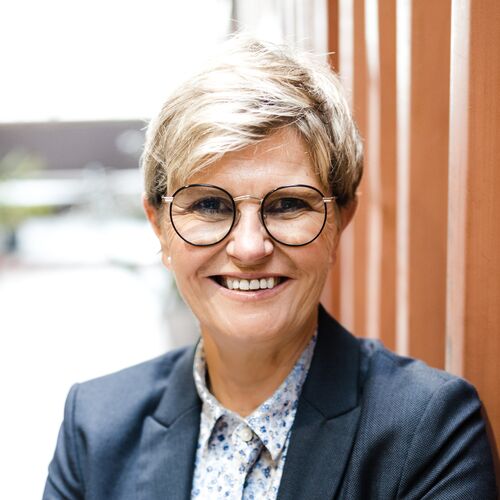 Kerstin Domin in dunkelblauem Blazer vor rostrotem Container im Coworking Space