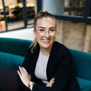 Lisa Garcia in schwarzem Blazer auf grünem Sofa im Coworking Space