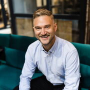 Markus Neumann in blauem Hemd auf dunkelgrünem Sofa in Coworking Space